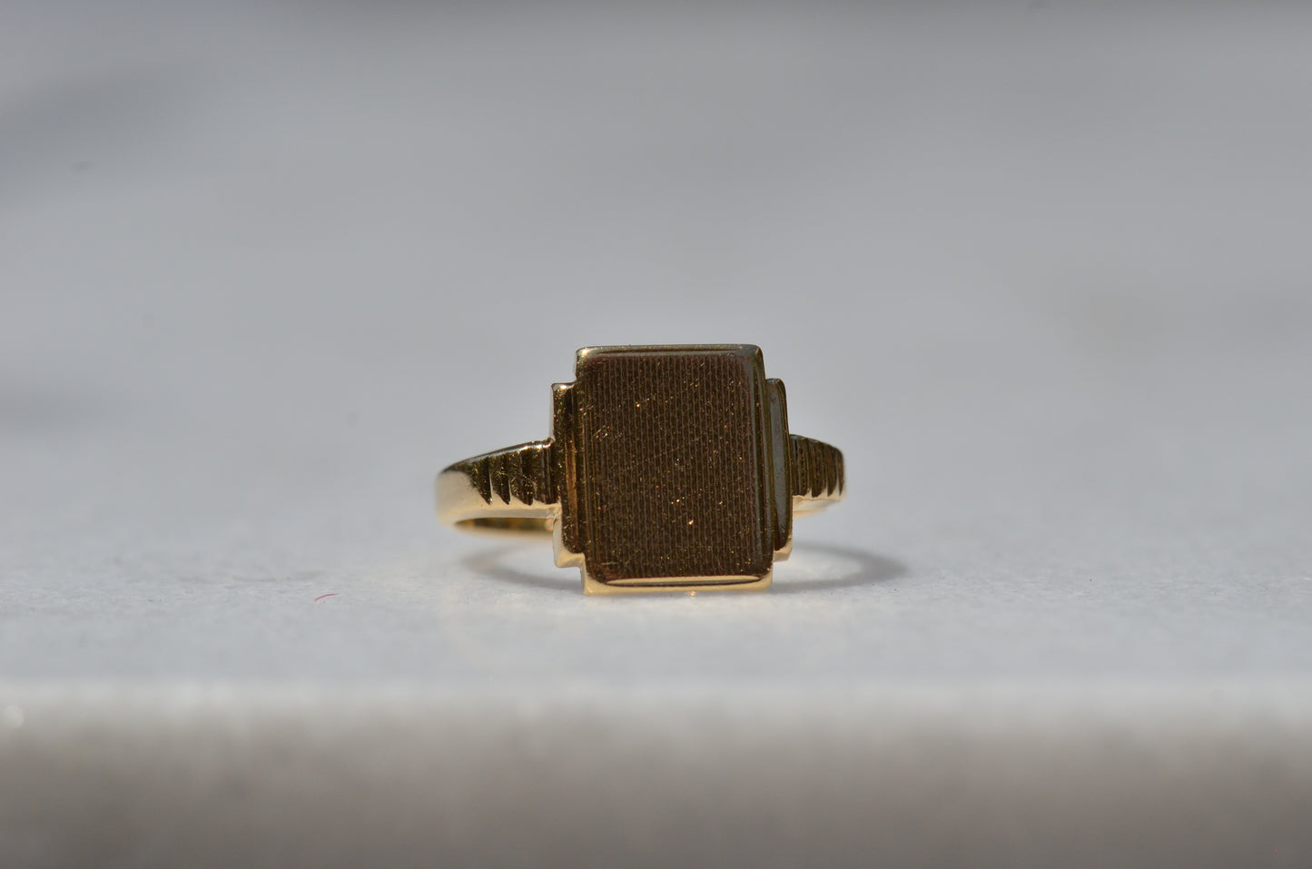 In diffused natural light, the wavy texture of the face of the signet is visible as well as light scratches and scuffs from nearly a century of wear. The ring is viewed turned slightly to the right, to better see the notched shoulders.