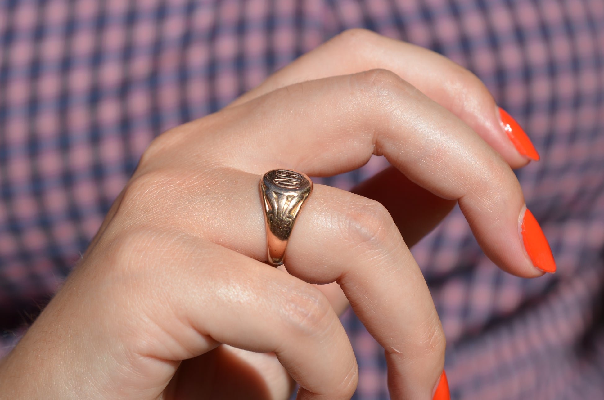 The ring is shown on the right ring finger of a Caucasian model in bright orangey-red nail polish.