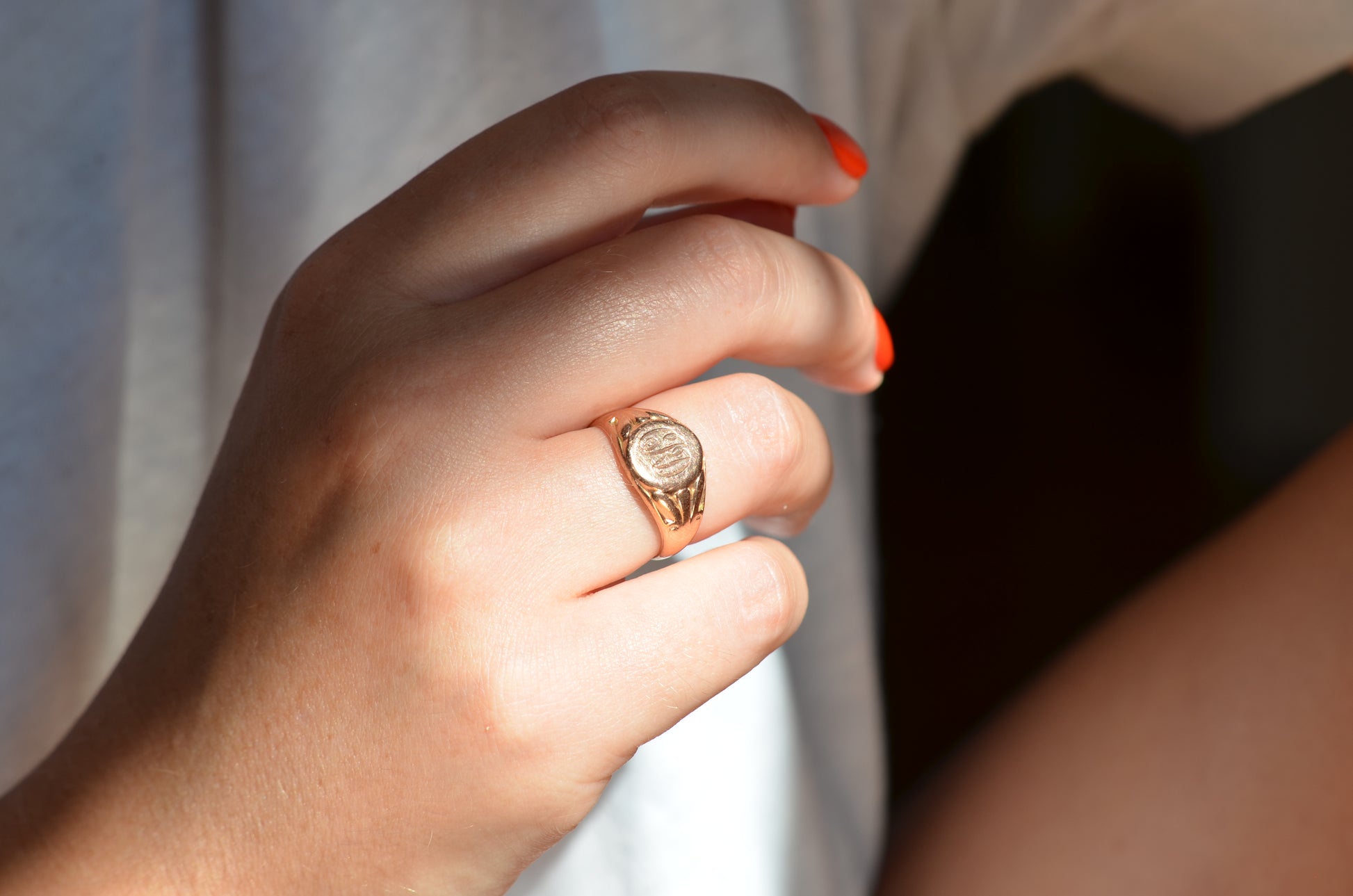 The ring is shown on the right ring finger of a Caucasian model in bright orangey-red nail polish.