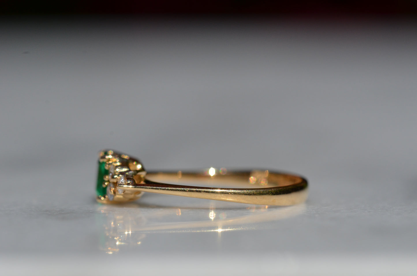 Close-cropped macro of a vintage ring, featuring a square emerald-cut emerald flanked by three round diamonds arranged in a triangular cluster on each shoulder. Viewed turned to the left to highlight the side of the band.