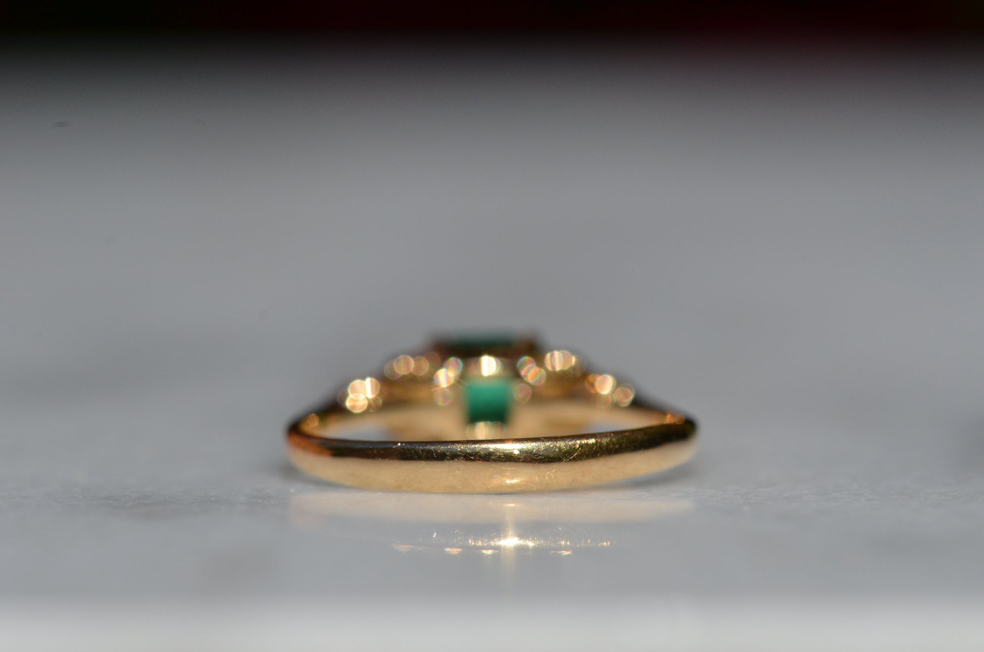 Close-cropped macro of a vintage ring, featuring a square emerald-cut emerald flanked by three round diamonds arranged in a triangular cluster on each shoulder. Viewed from the back to highlight the very good condition of the shank.