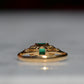 Close-cropped macro of a vintage ring, featuring a square emerald-cut emerald flanked by three round diamonds arranged in a triangular cluster on each shoulder. Viewed from the back focusing on the underside of the mount and back of the gemstones.