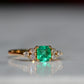 Close-cropped macro of a vintage ring, featuring a square emerald-cut emerald flanked by three round diamonds arranged in a triangular cluster on each shoulder. Viewed slightly to the right to highlight the diamond shoulders.
