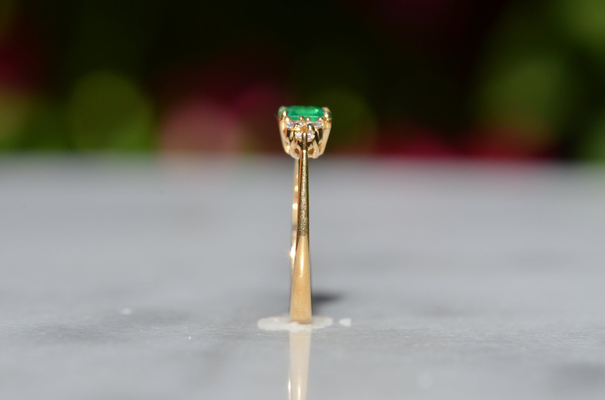 Close-cropped macro of a vintage ring, featuring a square emerald-cut emerald flanked by three round diamonds arranged in a triangular cluster on each shoulder. Viewed upright and from the side to highlight the profile.